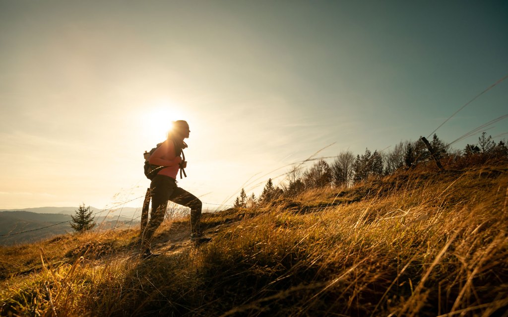 An active woman with a backpack hikes up a hill.