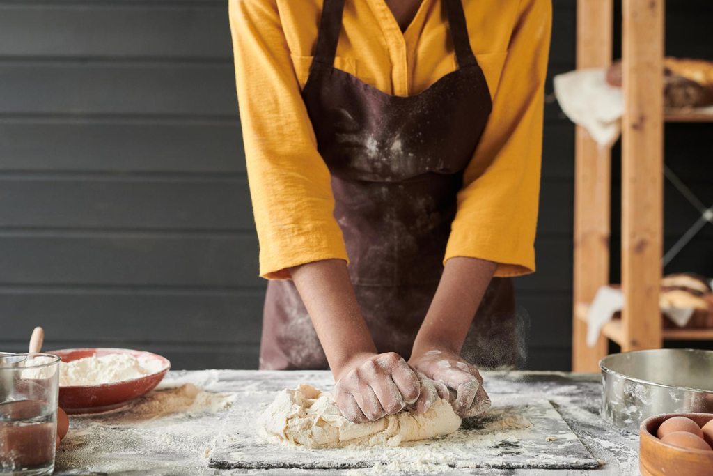 A baker rolls out dough on a countertop.