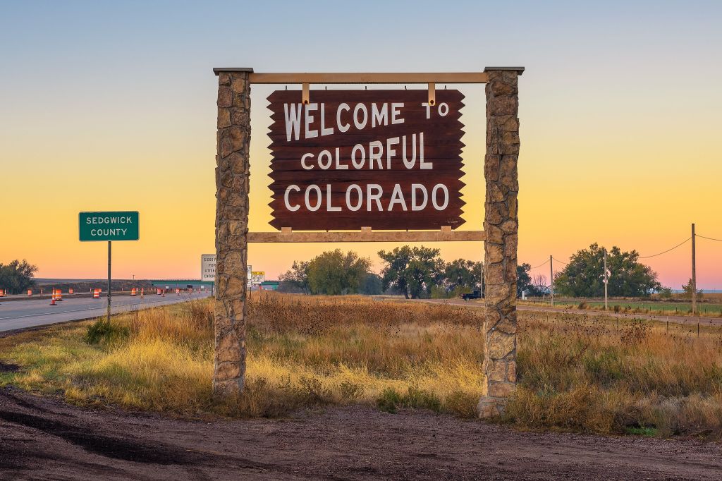 A large roadside sign saying 'Welcome to Colorful Colorado' with a sunset sky in the background