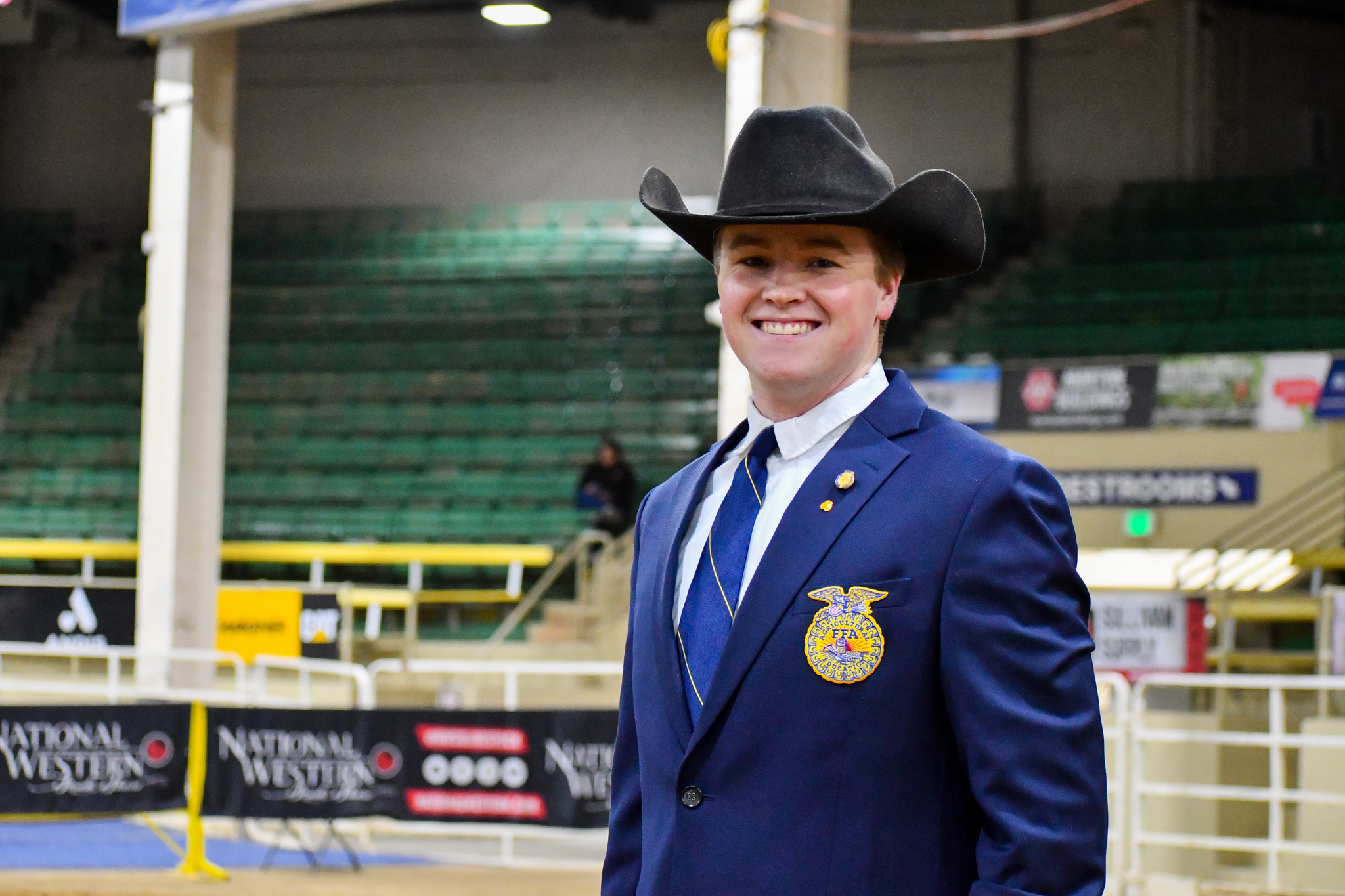 A photo of Harrison Falborn wearing an FFA jacket against the background of an indoor arena during National Western Stock Show.