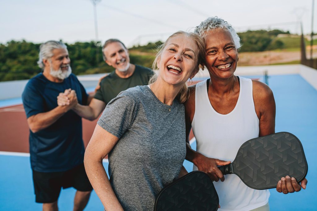 A group of older people smile as they finish a game of pickleball
