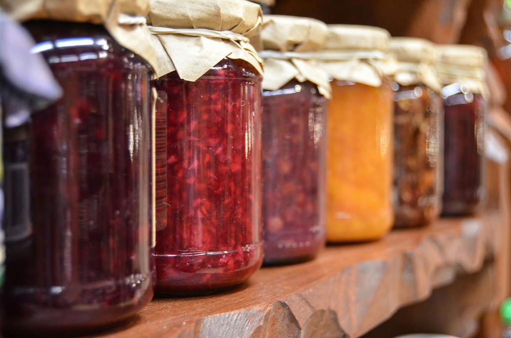 Jars of colorful homemade preserves lined up on a wooden shelf.