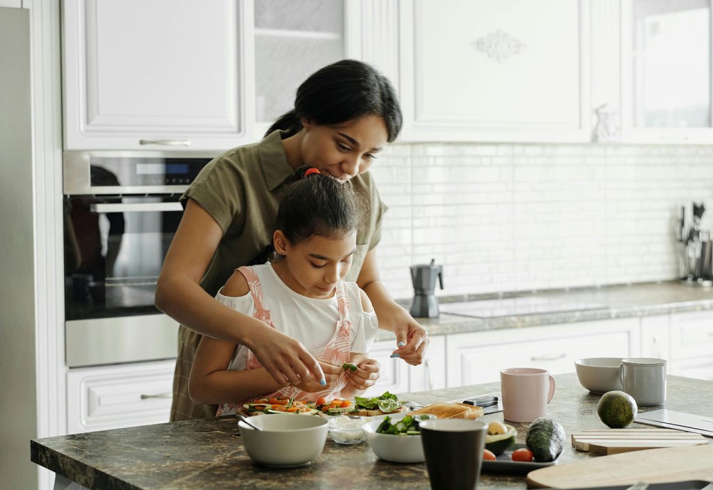 A mother and daughter preparing a meal together in a bright kitchen, smiling as they work.