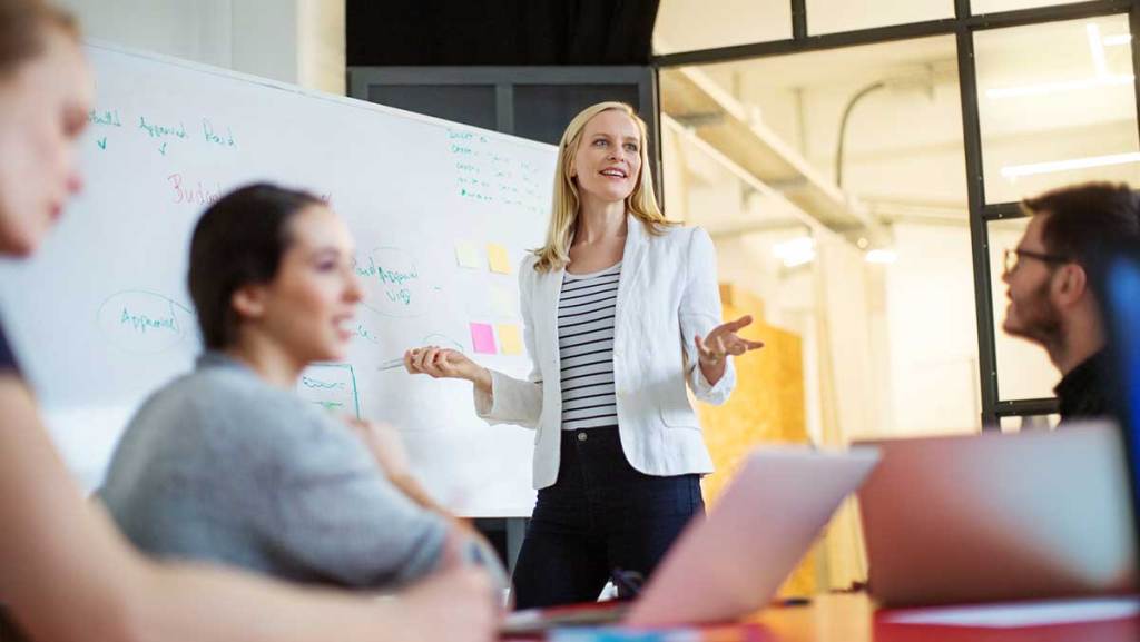 Woman presenting to a group of coworkers in a meeting room.