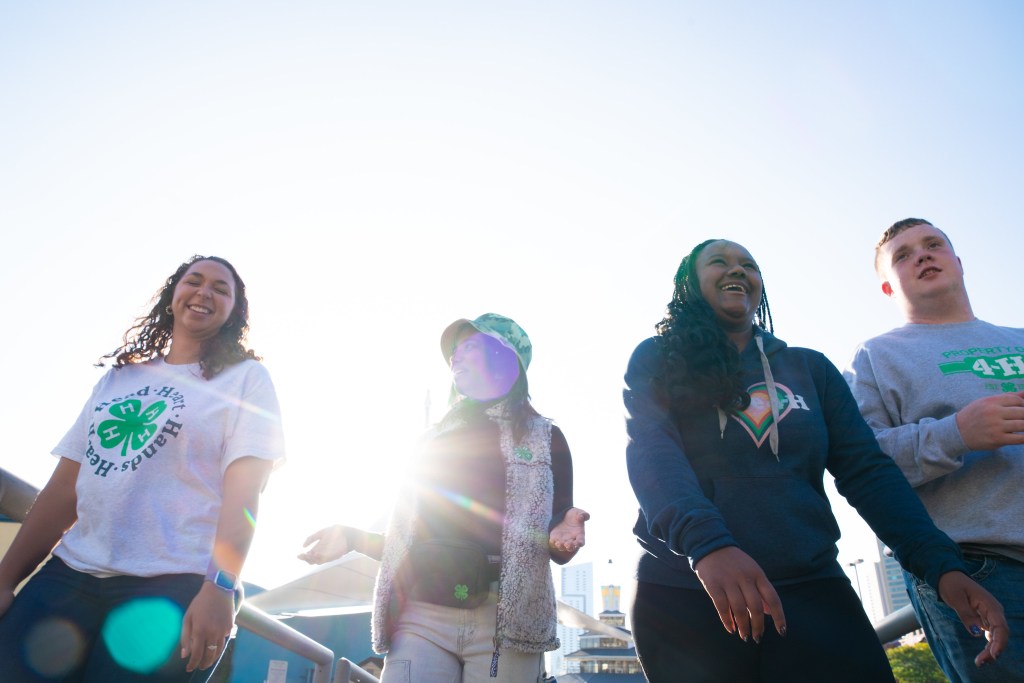 Four people smiling and walking together outdoors on a sunny day, with sunlight shining brightly behind them.