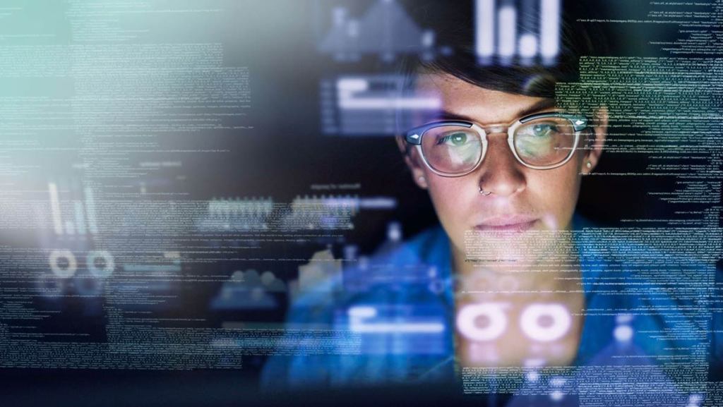 A woman staring into multiple screens where the reflection is seen on her glasses.