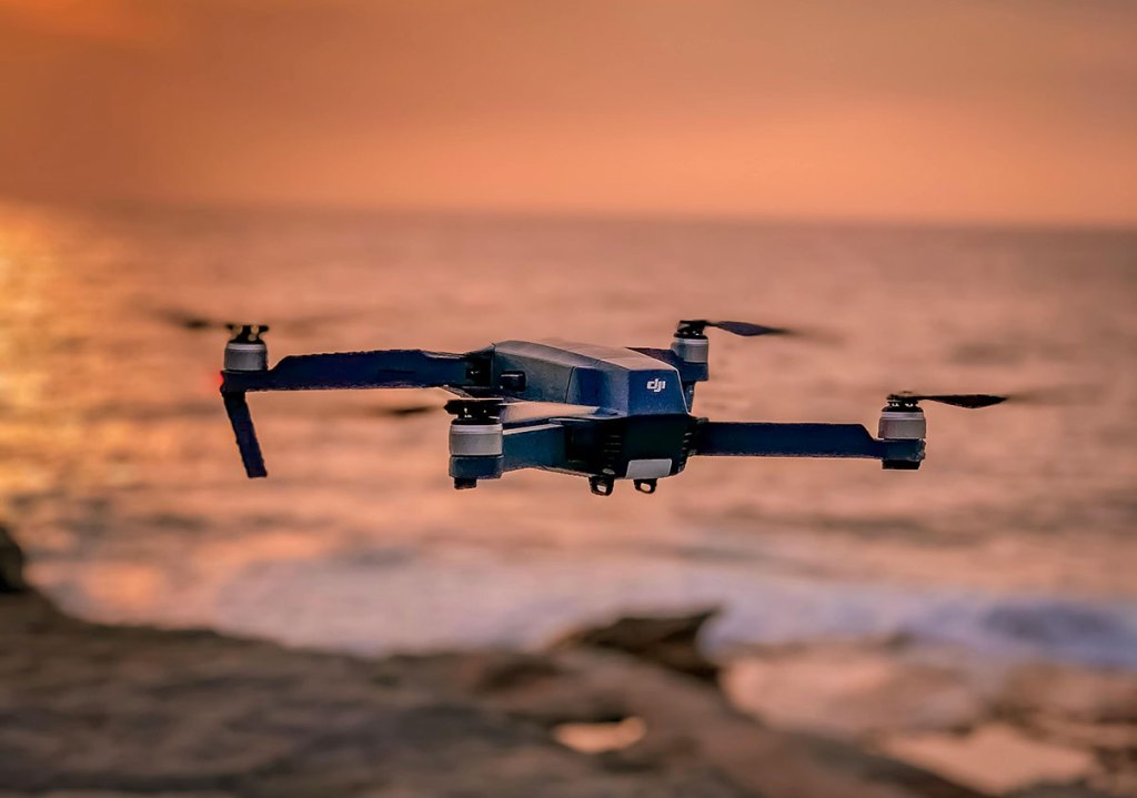 A drone hovering in the air with a sunset behind it.