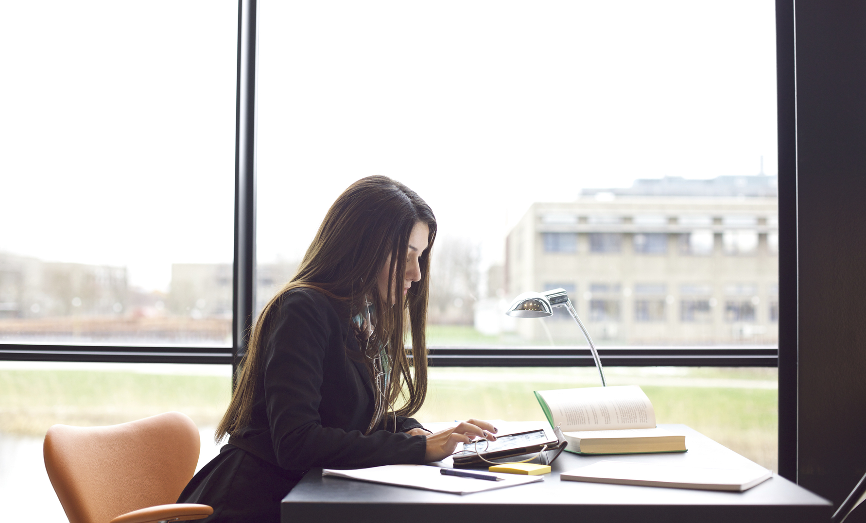 Woman sitting at a table with books and digital tablet.