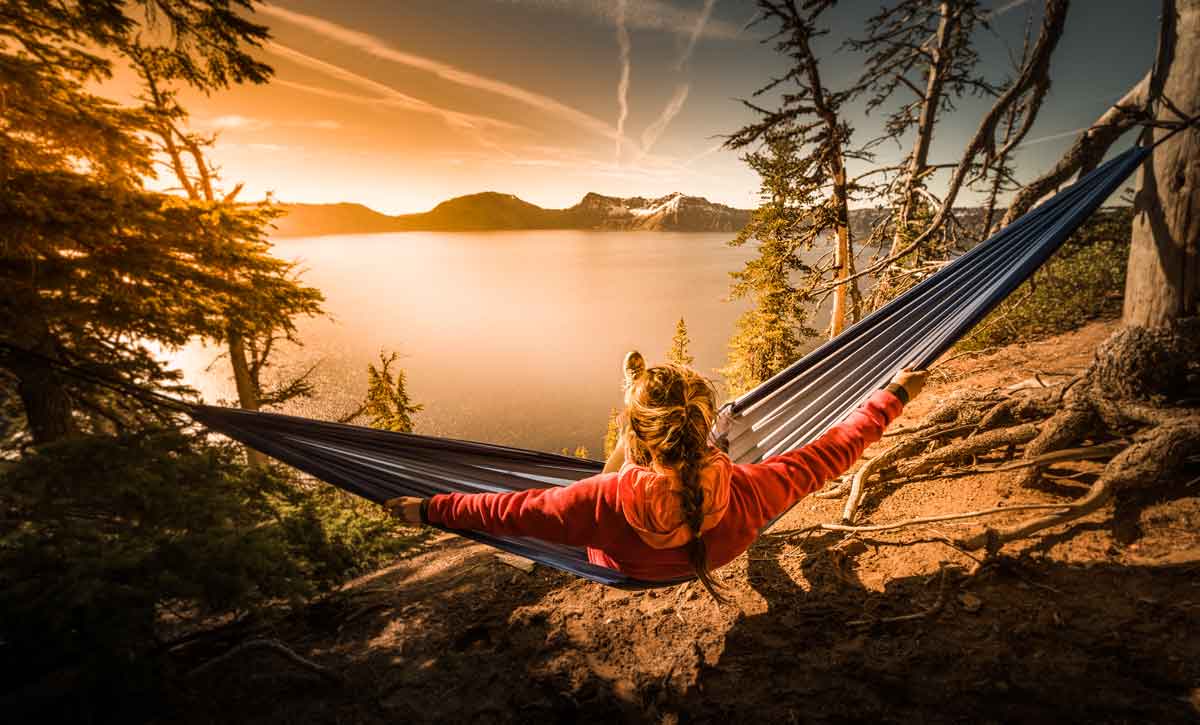 A person sitting on a hammock at sunset overlooking a lake.