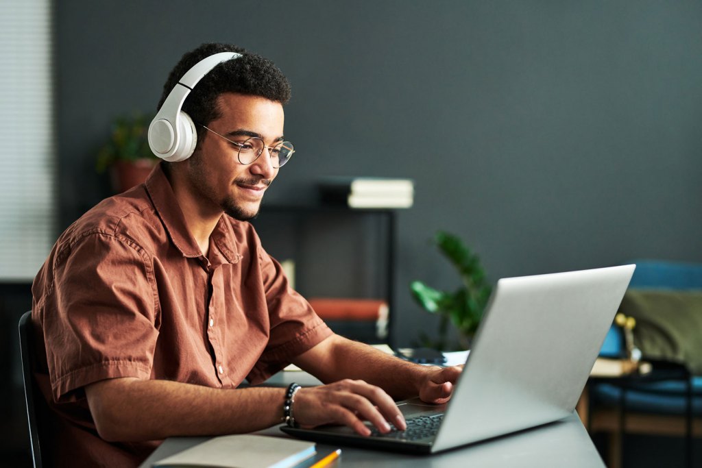 A young man studies on his computer with headphones.