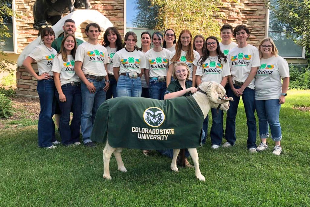 A group of students and a staff member from Colorado State University posing with CAM the Ram, the university's mascot, during a campus event.