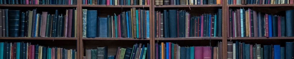 A bookshelf filled with a variety of books, mainly with dark-colored spines in shades of blue, green, red, and black.