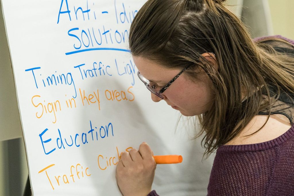 A young woman writing on a whiteboard filled with notes and ideas related to traffic solutions.