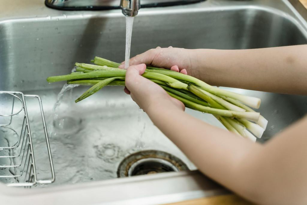 A person washing their food over the kitchen sink.