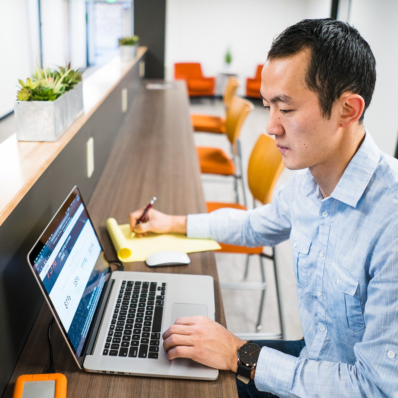 A man sitting at a table with a laptop writing on a notepad.