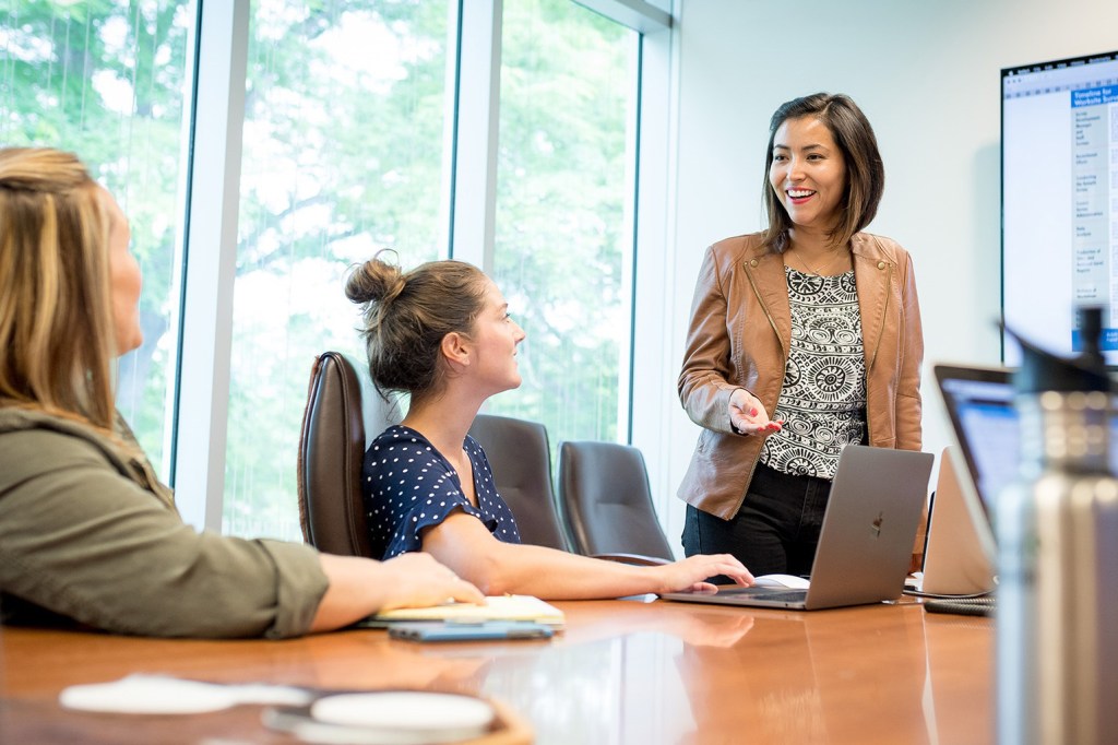 Woman speaking to coworkers during a meeting at a table.