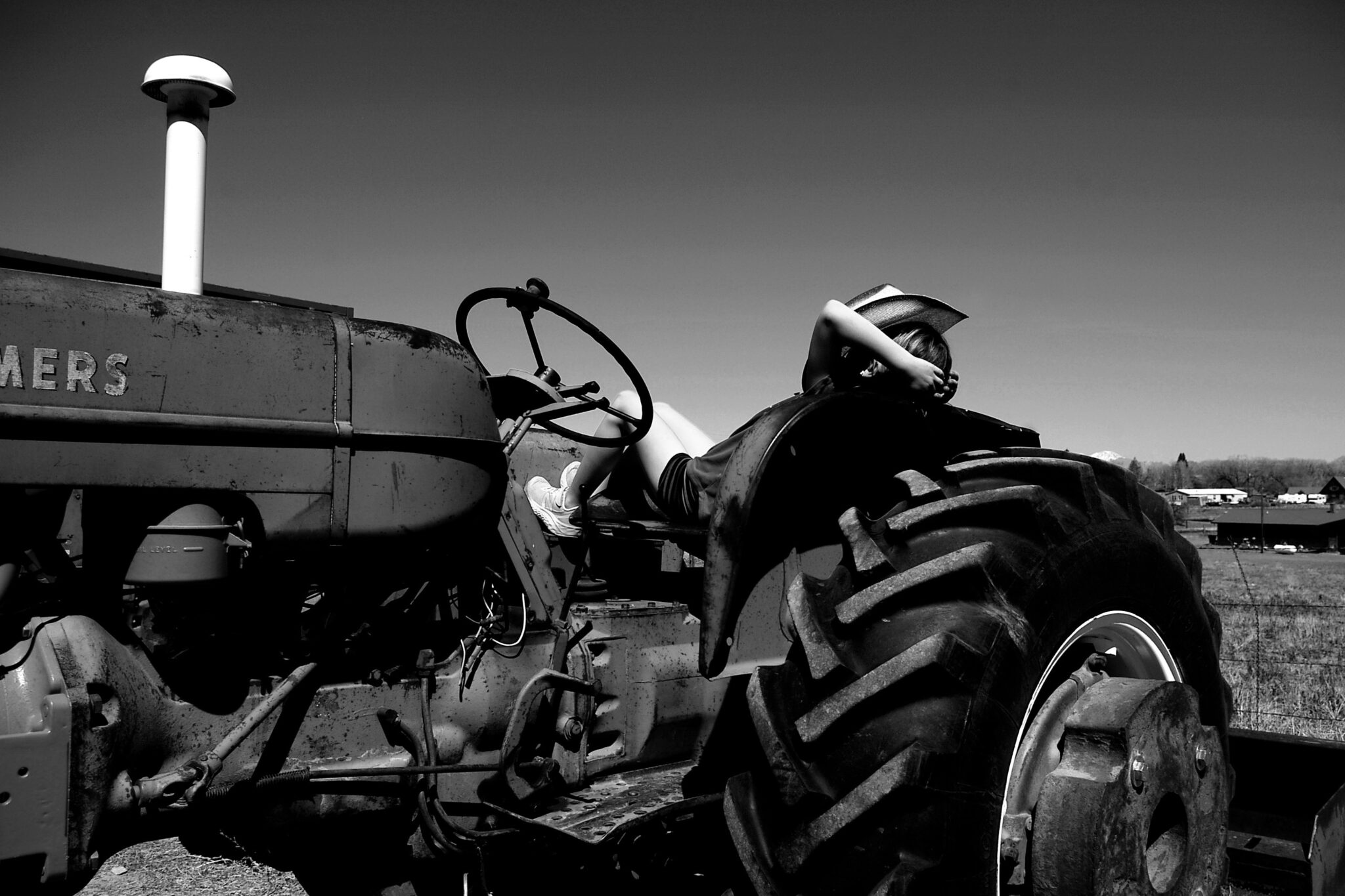 A black and white image of a person sitting on a tractor in an open field, gazing into the distance.