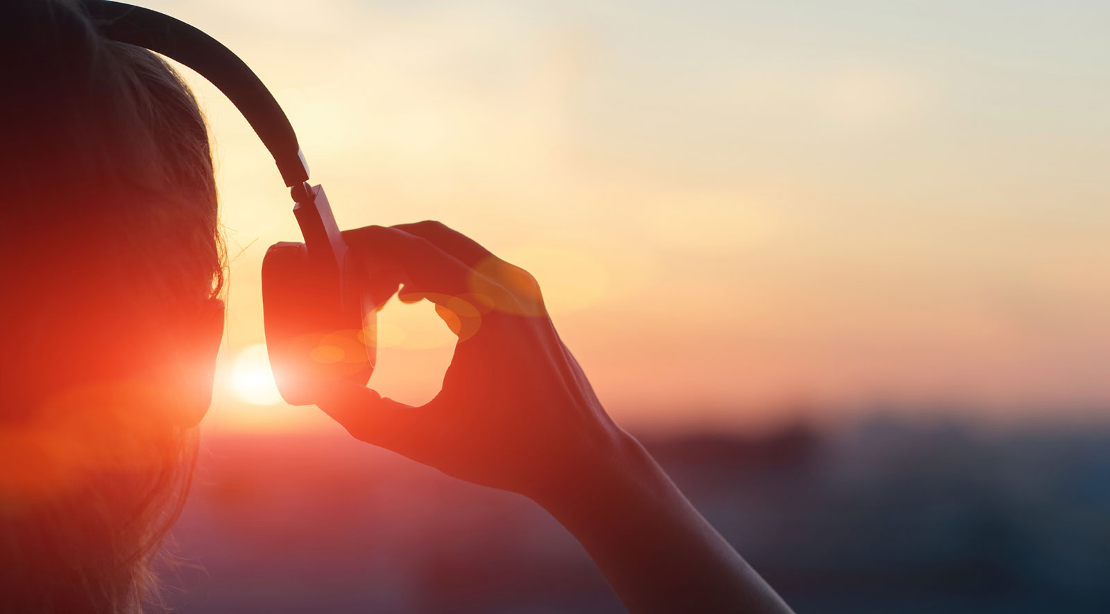 A person listening to headphones while watching a bright sunset, with the sun casting a warm glow over the scene.