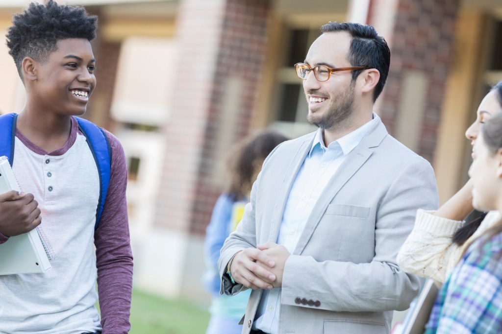 High school teacher talks with students outside on campus.